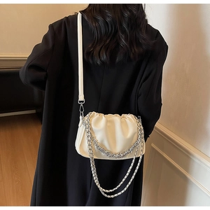 Close-up of white ruched bucket bag with silver metal chains on a black coat