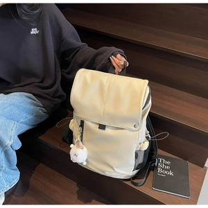 Detail of beige nylon backpack with plush charm on a wooden staircase setting