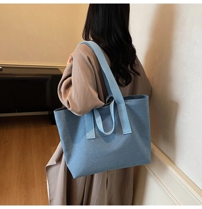 Detailed back view of a large blue canvas tote bag worn over the shoulder by a model
