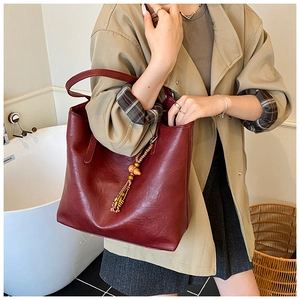Detail of burgundy leather tote bag with retro texture and unique wooden bead tassel