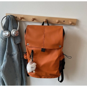 Detailed view of orange nylon backpack with a cute sheep plush charm on light wood hook