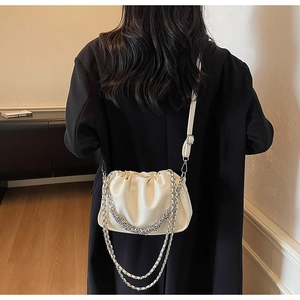 Detail view of white ruched hobo bag with metal chain and adjustable strap on a model