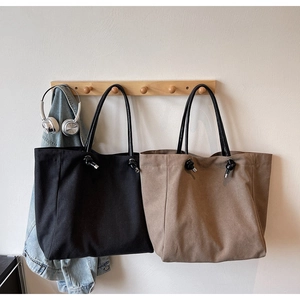 Detail of canvas tote bags in black and khaki with long handles and metal knot accents