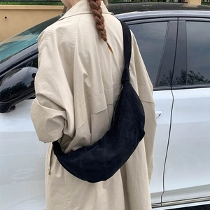 Detail of a black matte textured crossbody bag worn over a beige trench coat