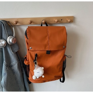 Detail of orange nylon backpack with cute sheep pendant and side mesh pocket hanging on a rack