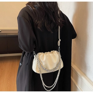 Detail of a beige pleated cloud bag with a silver chain strap on a black coat