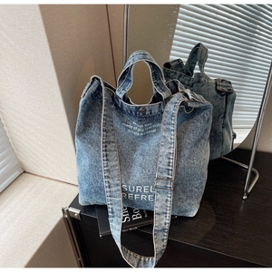 Detail of vintage washed denim tote bag with adjustable strap and white printed text