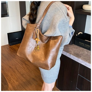 Close-up of brown leather tote bag featuring a wooden bead tassel and detailed stitching