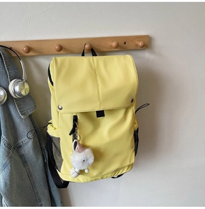 Detail of yellow nylon backpack with side mesh pockets and white fluffy pompom pendant