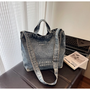 Blue denim tote bag with white typography placed next to a laptop in a cozy setting