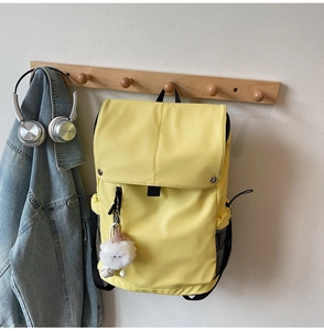 Bright yellow nylon backpack on a wall hook with a cute plush doll charm and headphones