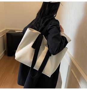 Detail of a large off-white canvas tote bag with black straps worn by a model in a room