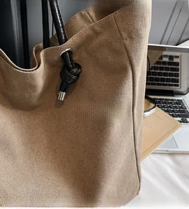 Detailed close-up of brown textured canvas tote bag with black knotted handle details
