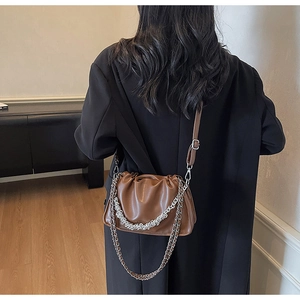 Detail of a brown ruched shoulder bag with silver chain strap worn over a black coat