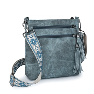 Detail of denim blue crossbody bag featuring multiple zippers, tassels, and a woven strap