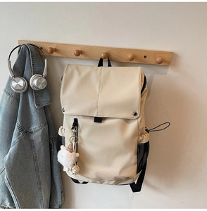 Detail of cream nylon backpack with plush charm and side mesh pocket hanging on wooden hook