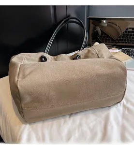 Close-up of khaki canvas tote bag featuring premium reinforced stitching and black leather handles