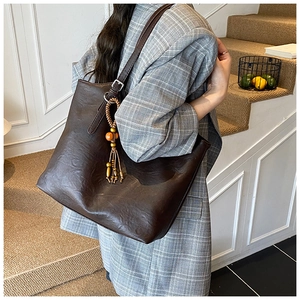 Macro detail of dark brown tote bag featuring retro wrinkled texture and beaded tassel