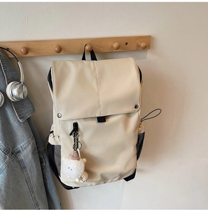 Detailed view of beige waterproof nylon backpack featuring a cute plush charm and pockets