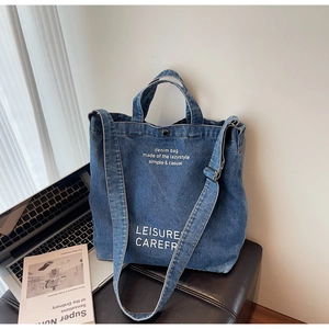 Detail of blue denim tote bag with white text, featuring adjustable straps and snap button