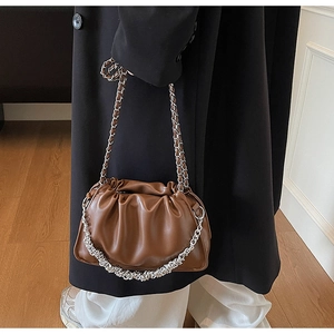 Detail of ruched brown leather bag with chunky silver chain on a shoulder model