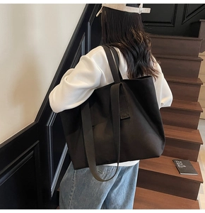 Model wearing a minimalist large black canvas tote bag in an indoor staircase setting