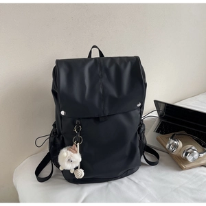 Black nylon backpack with white plush charm shown with laptop and books in a study setup