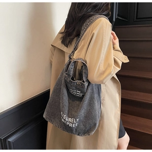 Detail view of grey denim tote bag with metal snap button worn over a trench coat