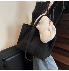 Detailed view of the large black tote bag carried by a model on a minimalist staircase