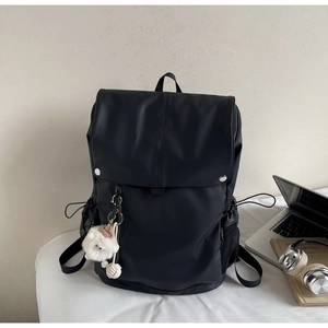 Close-up of black nylon backpack with metal buckles and cute white plush pendant accessory