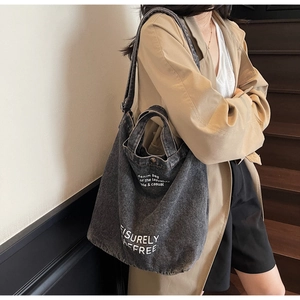 Close-up of a large denim tote bag in dark grey with white letter print on top