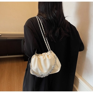 Detail of a creamy pleated cloud bag with stylish silver metal chain straps shown on a model