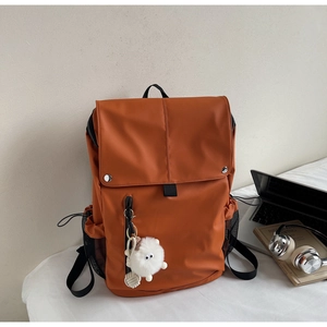 Detailed view of orange nylon backpack with plush charm, laptop and books on white cloth