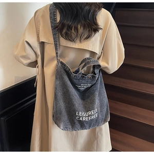 Detail of grey denim tote bag with Leisurely text held by model on wooden stairs