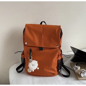 Detailed view of an orange nylon backpack featuring a plush charm and side mesh pockets