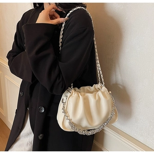 Close-up of ivory pleated cloud bag with silver metal chain on black suit