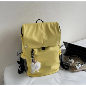 Macro view of a yellow nylon backpack with side pockets and a plush monster keychain