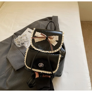 Detail of a vintage black leather backpack featuring white lace trim and a large bow