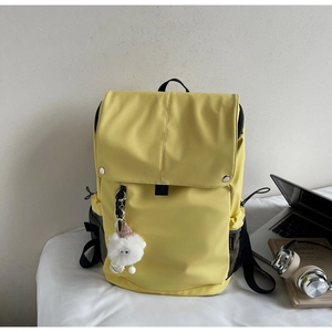 Detail of yellow nylon backpack with side mesh pocket, open flap and a plush bear charm