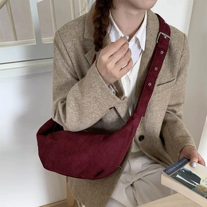 Side view of a dark red matte suede half-moon crossbody bag styled on a beige wool blazer