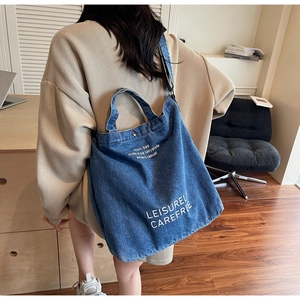 Rear view of a dark blue denim tote bag with LEISURELY CAREFREE print on a model