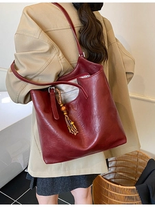 Large burgundy tote bag with wood bead tassel shown on model in a stylish indoor setting
