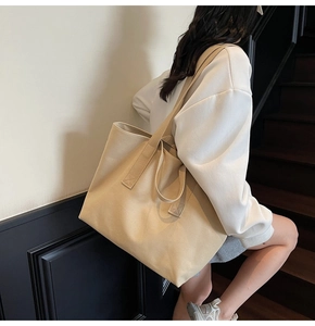Detail of a large beige canvas tote bag with dual handles for shoulder and hand carry