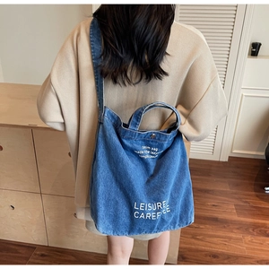 Detail of denim tote bag with white lettering back view on a female model
