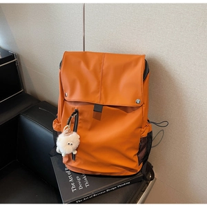 Detail of orange nylon backpack with dual buckles and cute white plush charm on side