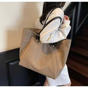 Detailed side view of khaki large tote bag with black leather handles and metal buckle