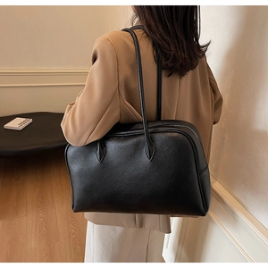 Dettaglio della borsa tote grande in pelle nera a grana indossata su un blazer cammello