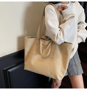 Detailed view of beige canvas tote bag worn by a model in a minimalist indoor setting
