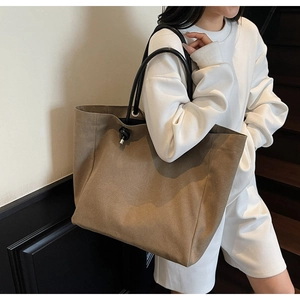 Close-up of a large tan canvas tote bag with black tubular handles on a fashion model