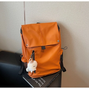 Detail of orange nylon backpack with metal snap buttons and cute plush sheep pendant